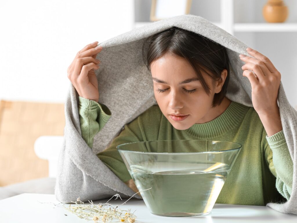 woman inhaling essential oils aromatherapy from a steam bowl of hot water