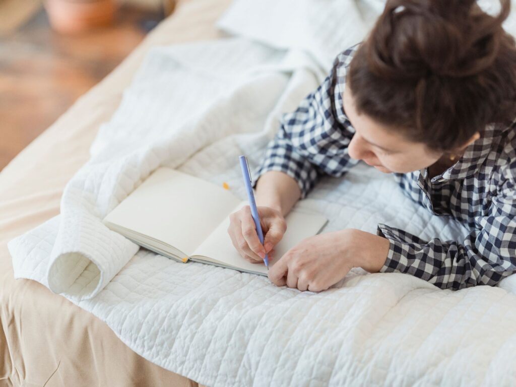 woman lying on bed writing in journal